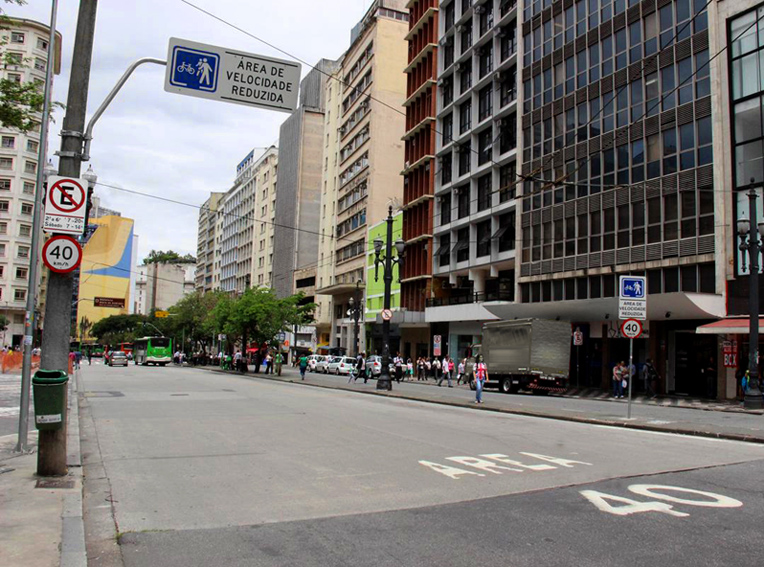 Imagem mostra uma rua com vários prédios e alguns carros